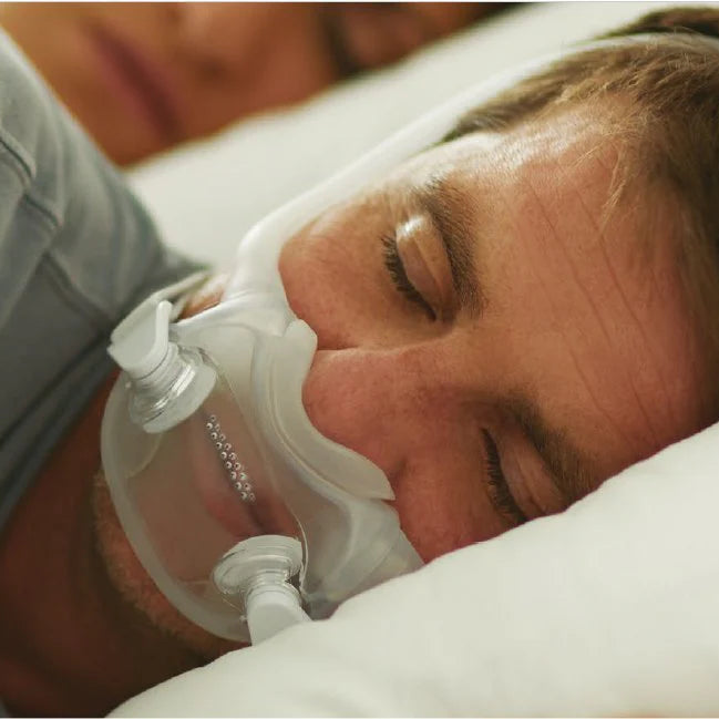 A person sleeping comfortably wearing a Philips Respironics full face CPAP mask with headgear.